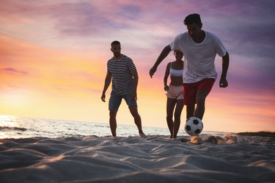 Friends playing football on beach at sunset