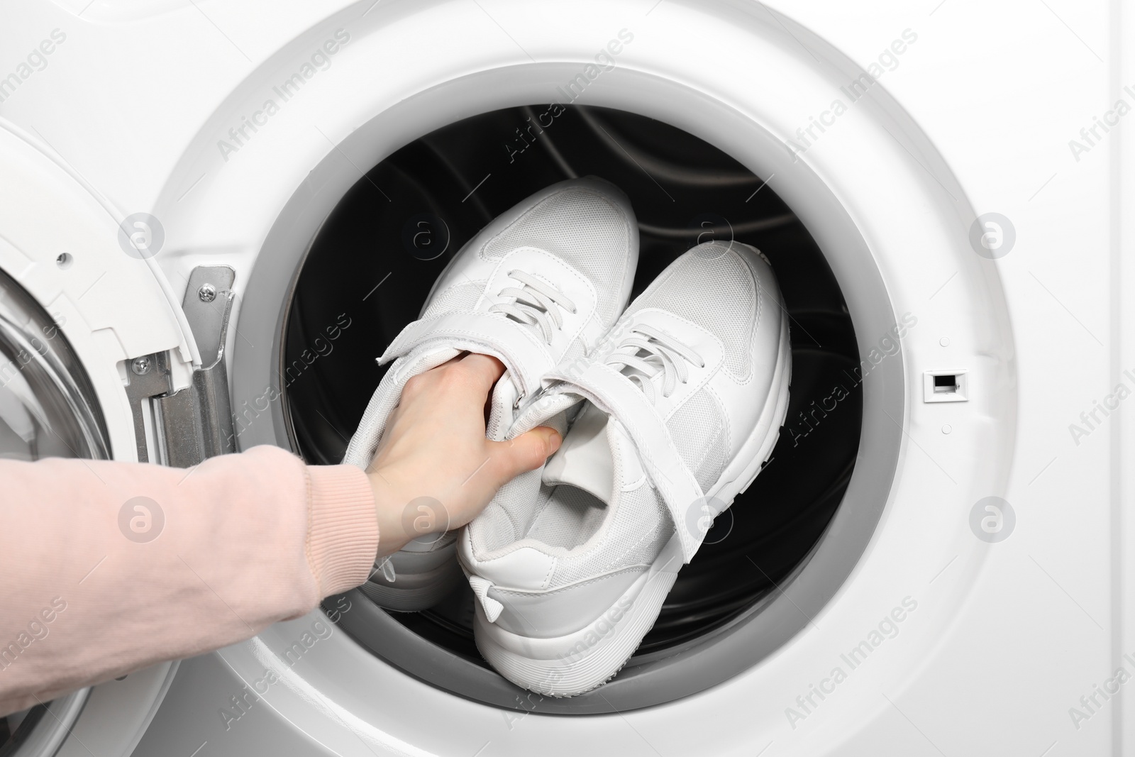 Photo of Woman putting stylish sneakers into washing machine, closeup