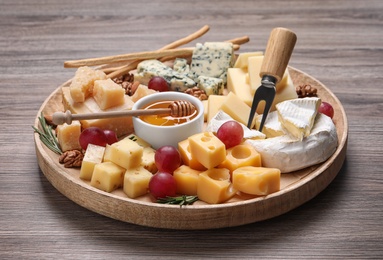 Photo of Cheese plate with honey, grapes and nuts on wooden table