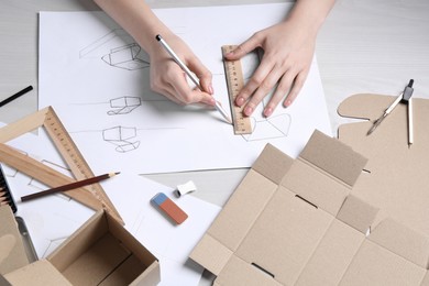 Woman creating packaging design at light wooden table, above view