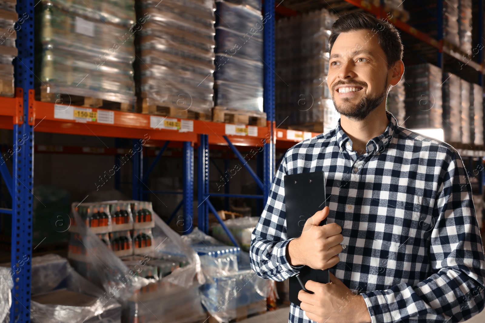 Photo of Happy manager holding clipboard in warehouse with lots of products. Space for text