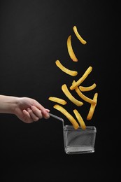 French fries falling into metal basket held by woman on black background, closeup