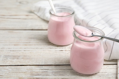 Photo of Glass jars with creamy yogurt served on white wooden table. Space for text