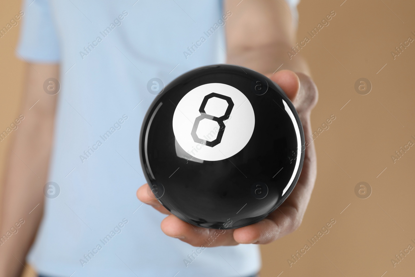 Photo of Man holding magic eight ball on light brown background, closeup