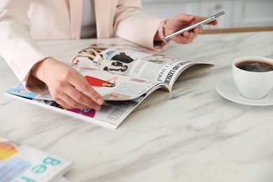 Woman with mobile phone and coffee reading fashion magazine at white marble table, closeup