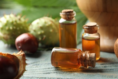 Photo of Chestnuts and bottles of essential oil on blue wooden table, closeup