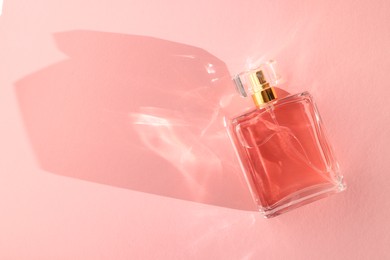 Photo of Luxury women's perfume. Sunlit glass bottle on pink background, top view. Space for text