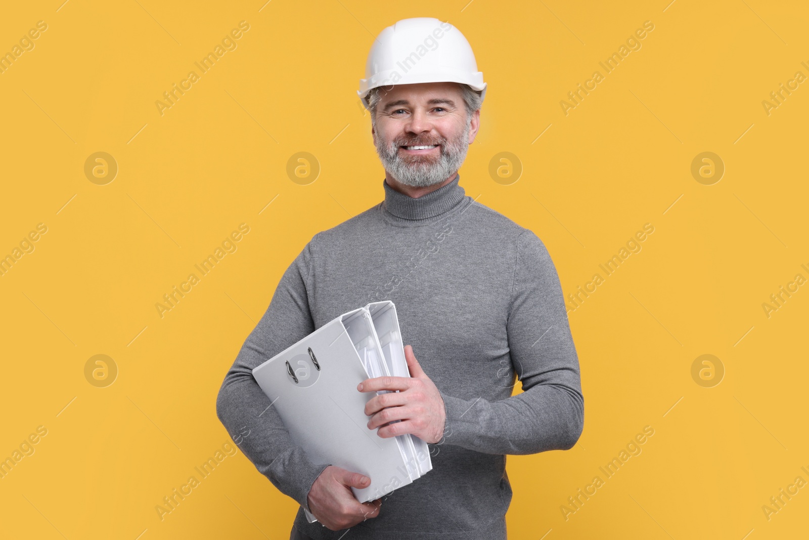 Photo of Architect in hard hat holding folders on orange background