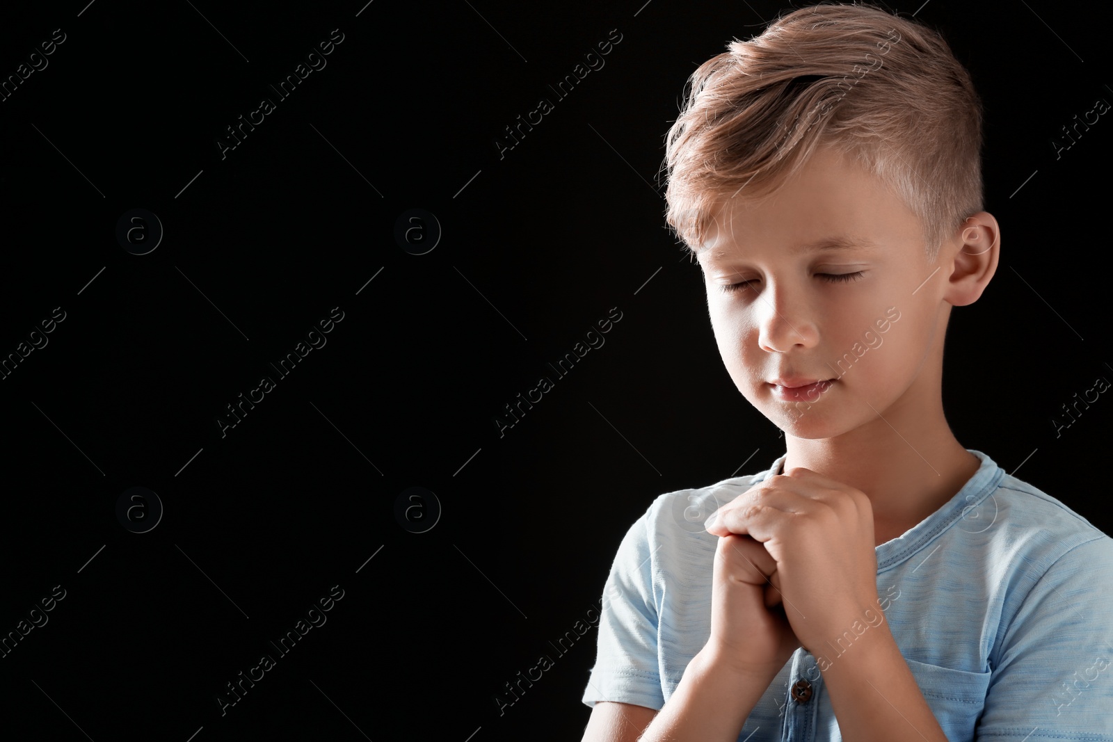 Photo of Little boy with hands clasped together for prayer on black background. Space for text