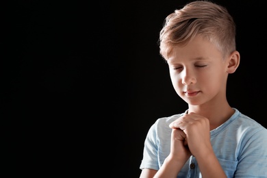 Photo of Little boy with hands clasped together for prayer on black background. Space for text