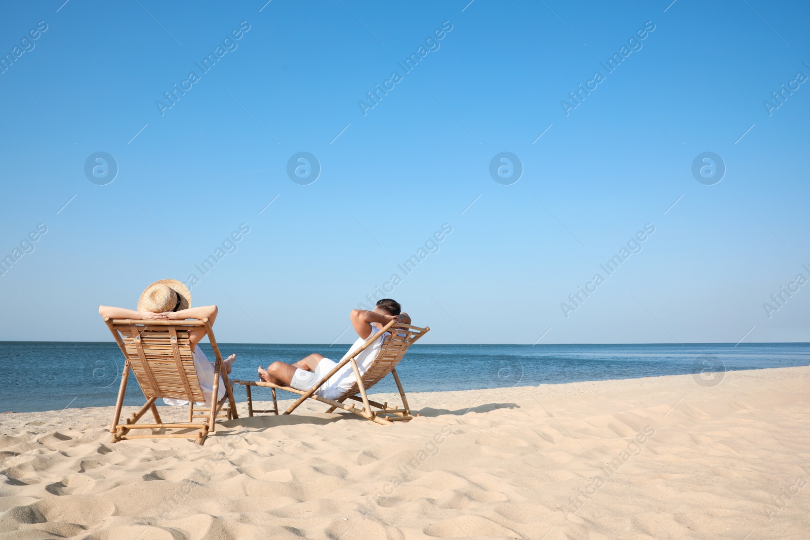 Photo of Young couple relaxing in deck chairs on beach