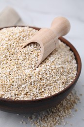 Photo of Dry barley groats and scoop in bowl on white table, closeup