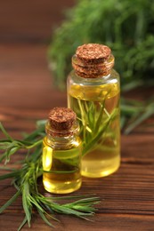 Photo of Bottles of essential oil and fresh tarragon leaves on wooden table