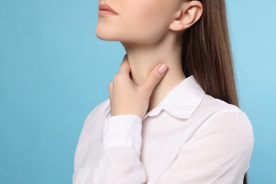 Photo of Woman with sore throat on light blue background, closeup. Space for text