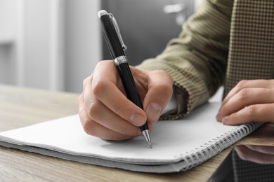 Photo of Woman writing in notebook at wooden table indoors, closeup