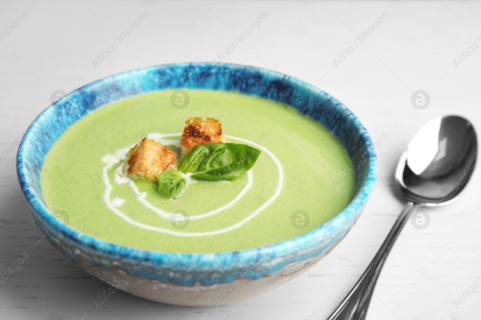 Photo of Delicious broccoli cream soup with croutons served on white wooden table