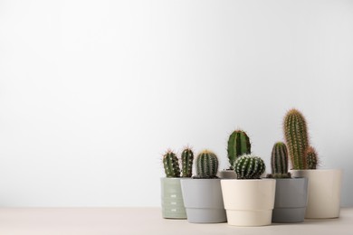 Different cacti in pots on beige table, space for text