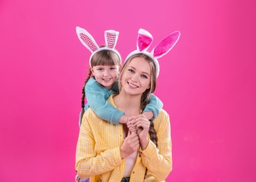 Happy woman and daughter with bunny ears on color background