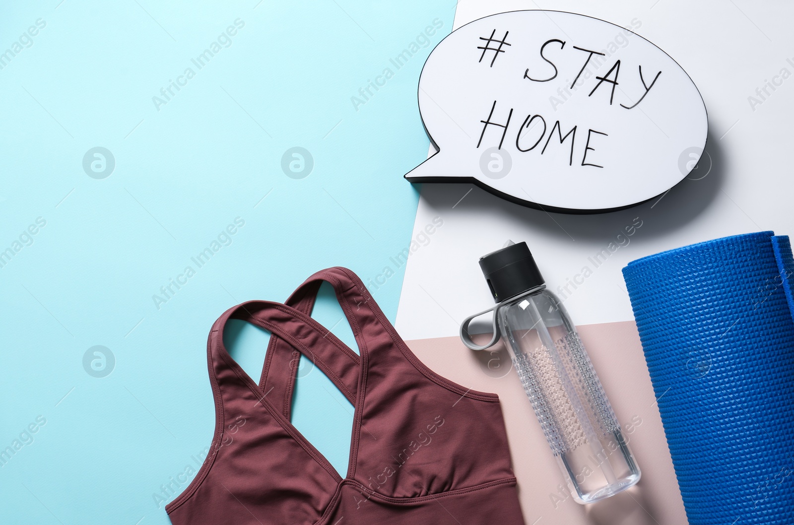 Photo of Stylish sportswear, yoga mat and speech bubble with hashtag Stay at Home on color background, flat lay. Self isolation during COVID‑19 pandemic