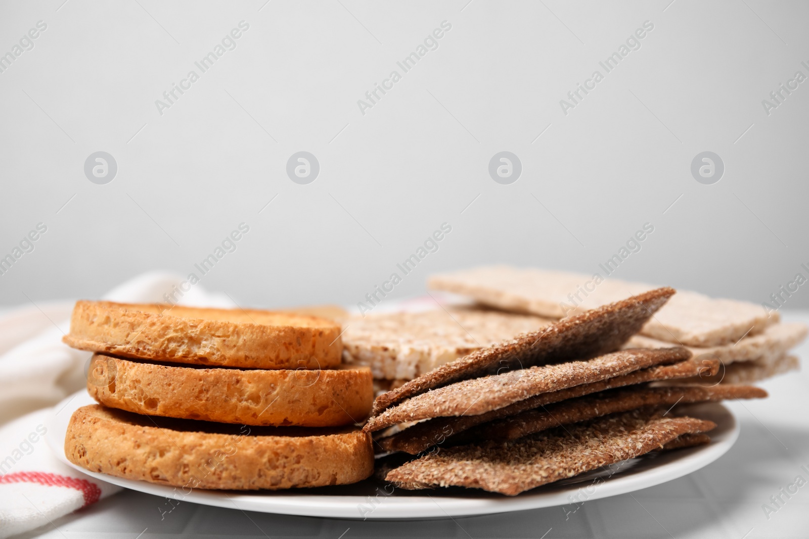 Photo of Plate of rye crispbreads, rice cakes and rusks on white table, space for text