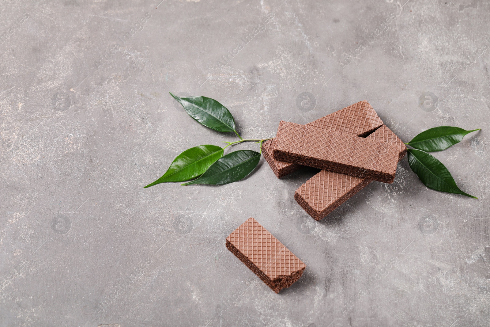 Photo of Delicious chocolate wafers with leaves on grey stone background. Space for text