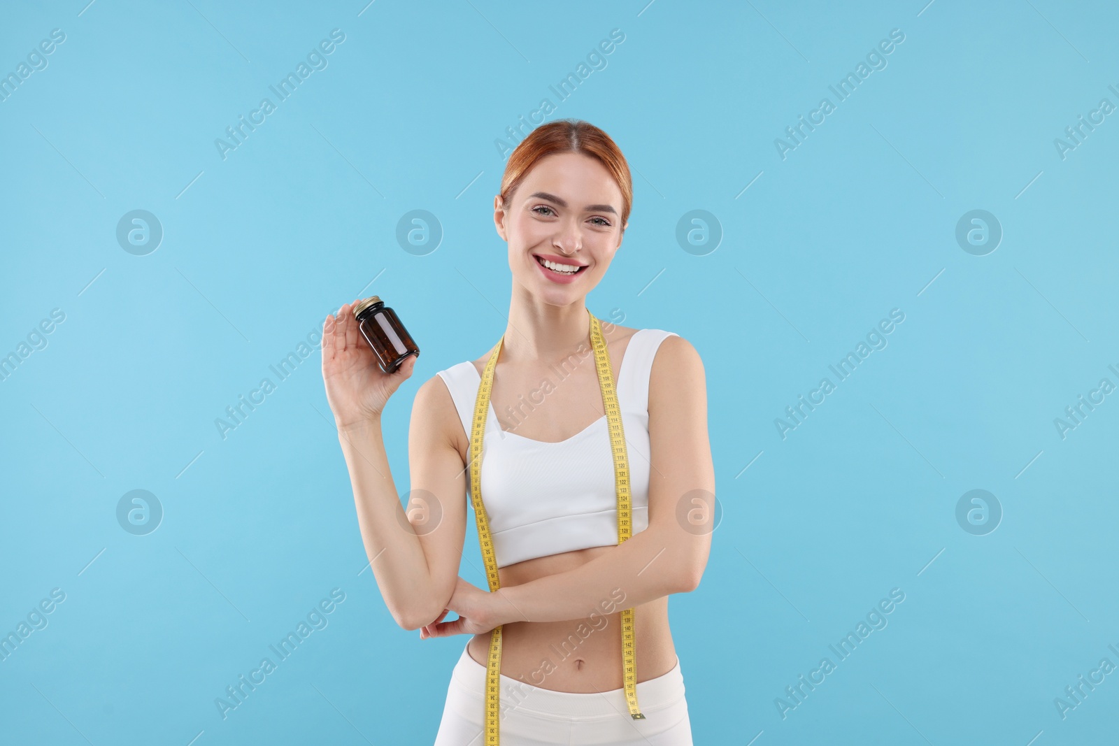 Photo of Happy young woman with bottle of pills and measuring tape on light blue background. Weight loss