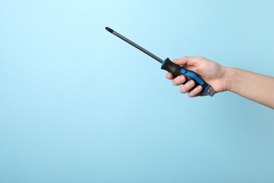 Photo of Woman holding screwdriver on light blue background, closeup. Space for text