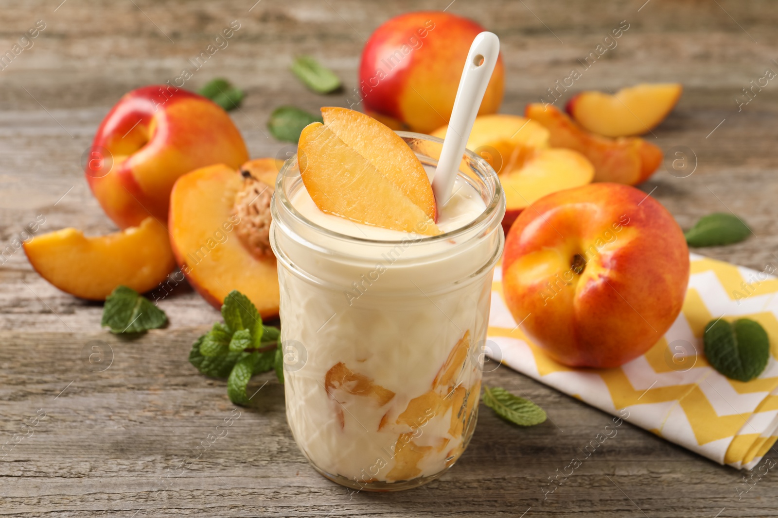 Photo of Tasty peach yogurt with pieces of fruit and spoon in glass jar on wooden table