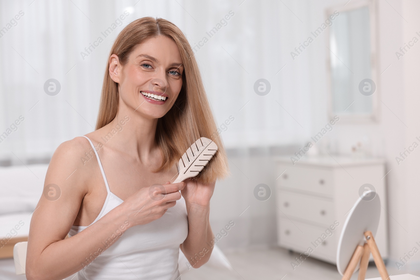 Photo of Beautiful happy woman brushing her hair in bedroom. Space for text