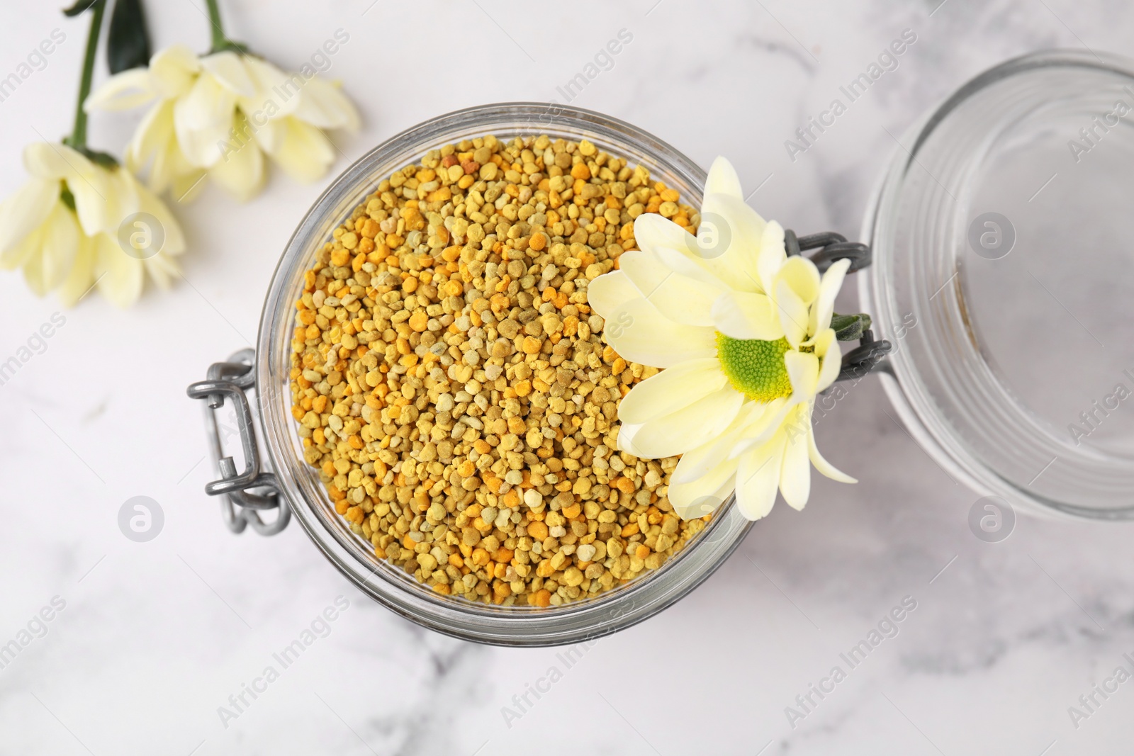 Photo of Fresh bee pollen granules in jar and flowers on light table, top view