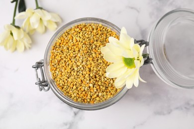 Fresh bee pollen granules in jar and flowers on light table, top view