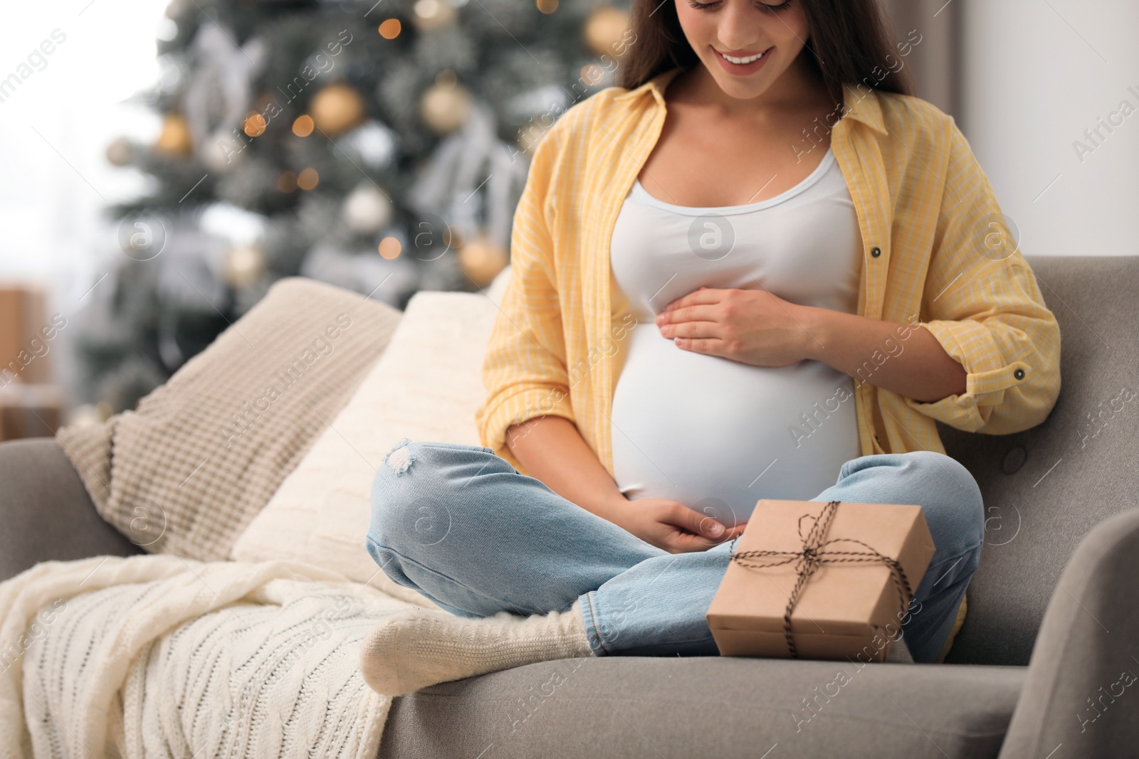 Photo of Happy pregnant woman with gift box in living room decorated for Christmas, closeup. Expecting baby