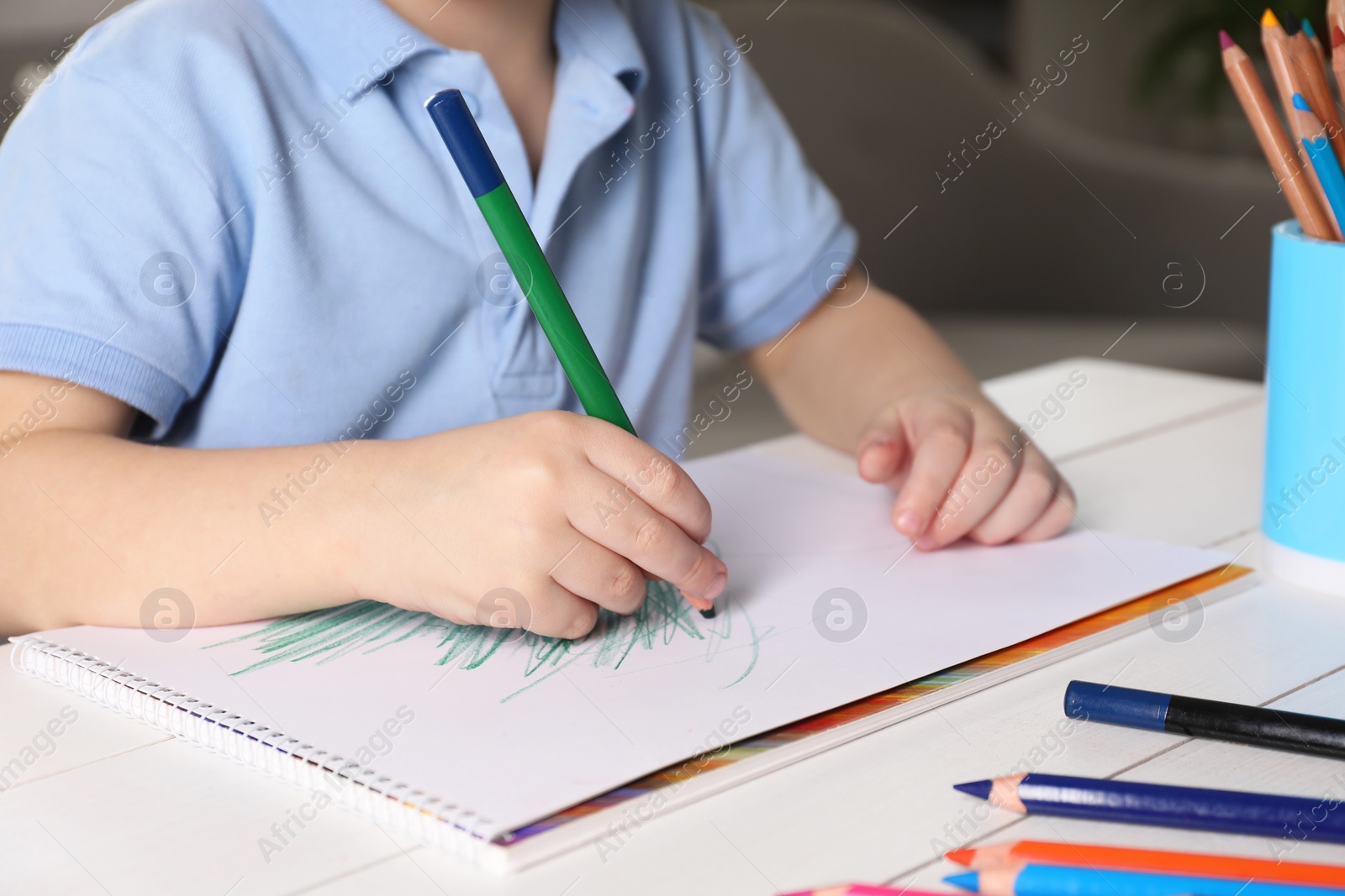 Photo of Little boy drawing with pencil at white wooden table indoors, closeup. Child`s art