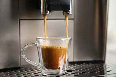 Espresso machine pouring coffee into glass cup, closeup