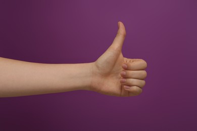 Photo of Woman showing thumb up on purple background, closeup