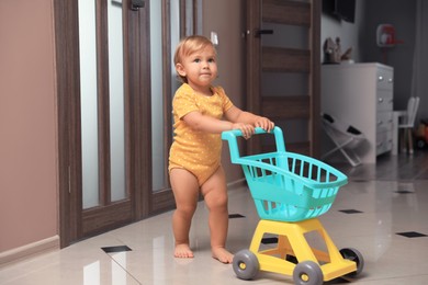 Cute baby with toy walker in room. Learning to walk