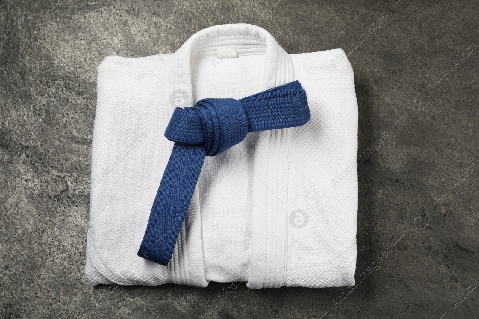 Photo of Blue karate belt and white kimono on gray textured background, top view