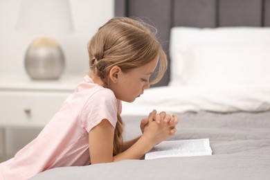 Girl holding hands clasped while praying over Bible in room