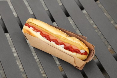 Fresh delicious hot dog with sauce on black bench outdoors