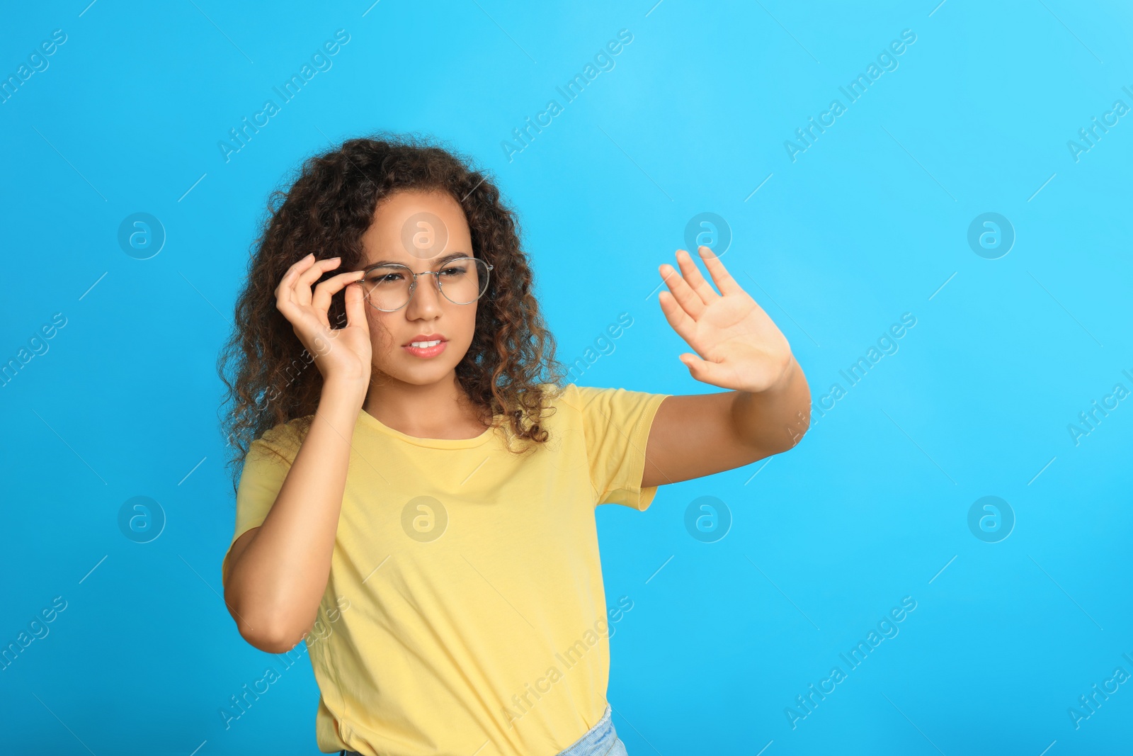 Photo of Young African-American woman with glasses on blue background. Vision problems