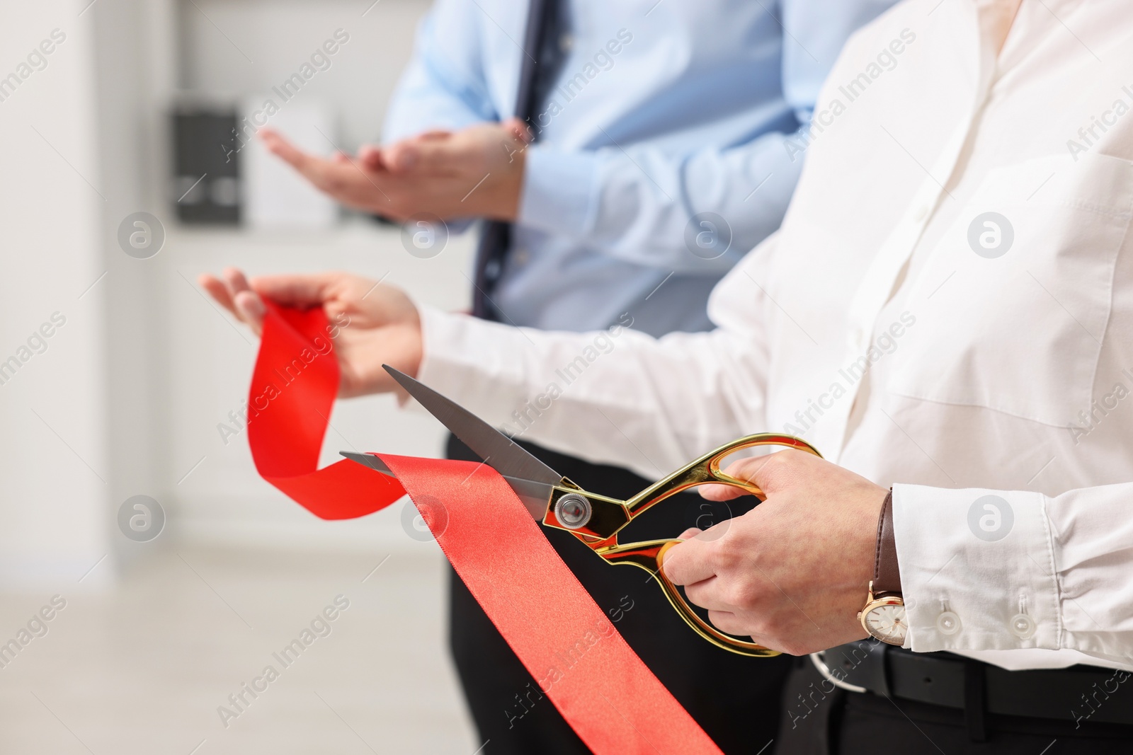 Photo of Woman cutting red ribbon with scissors indoors, closeup