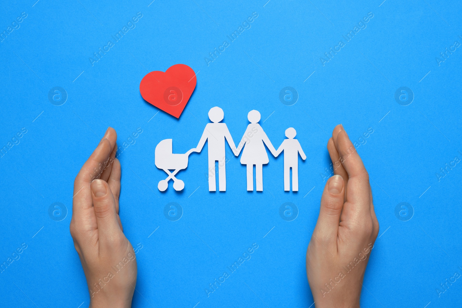 Photo of Woman protecting paper family cutout on light blue background, top view. Insurance concept