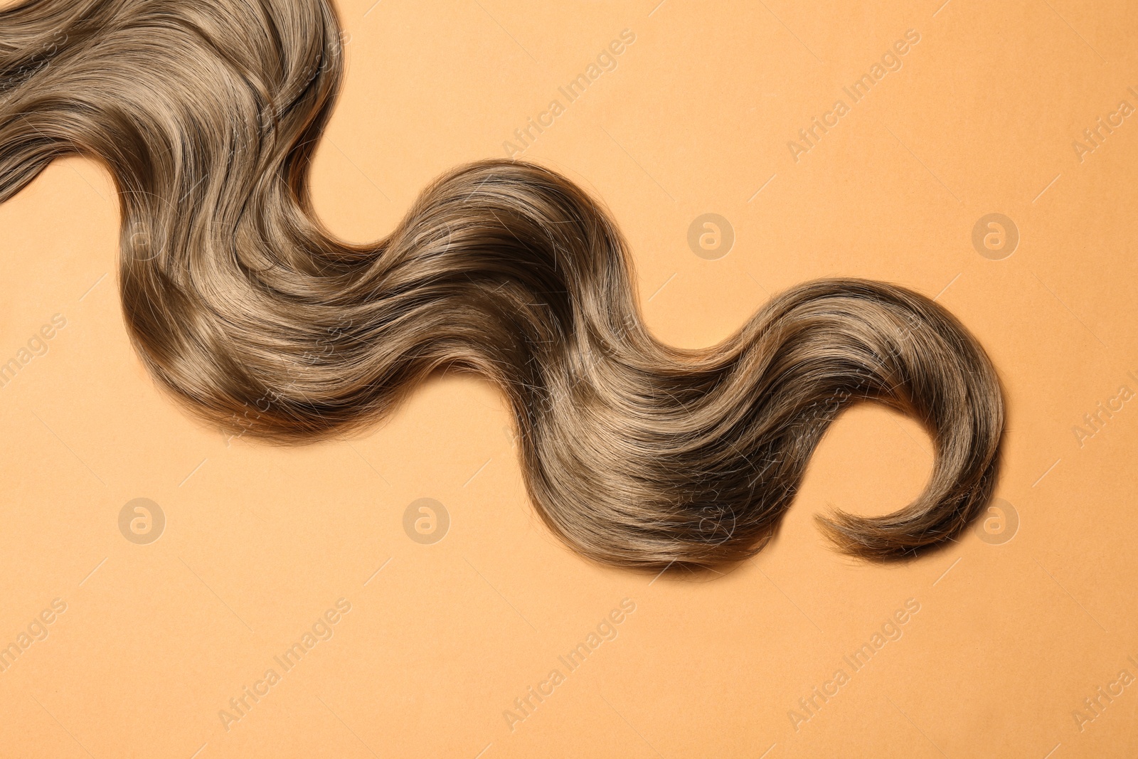 Photo of Lock of brown wavy hair on color background, top view
