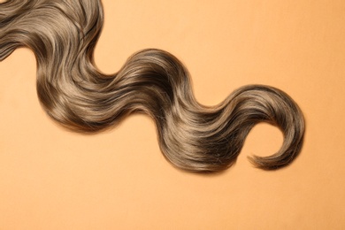 Lock of brown wavy hair on color background, top view