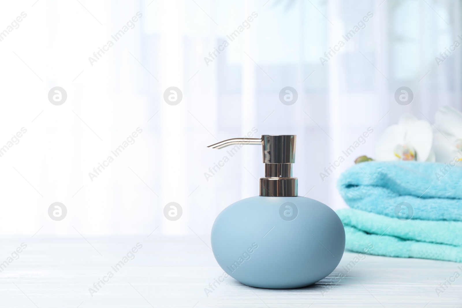 Photo of Stylish soap dispenser with flowers and towels on table. Space for text
