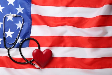 Photo of Stethoscope and red heart on American flag, flat lay. Space for text