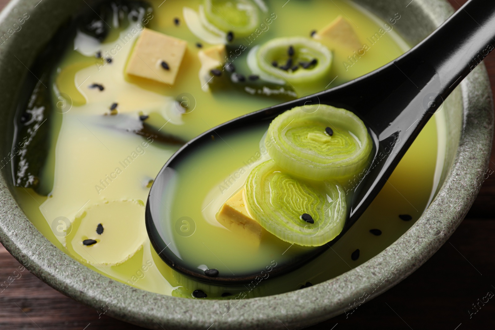 Photo of Bowl of delicious miso soup with tofu and spoon on wooden table, closeup