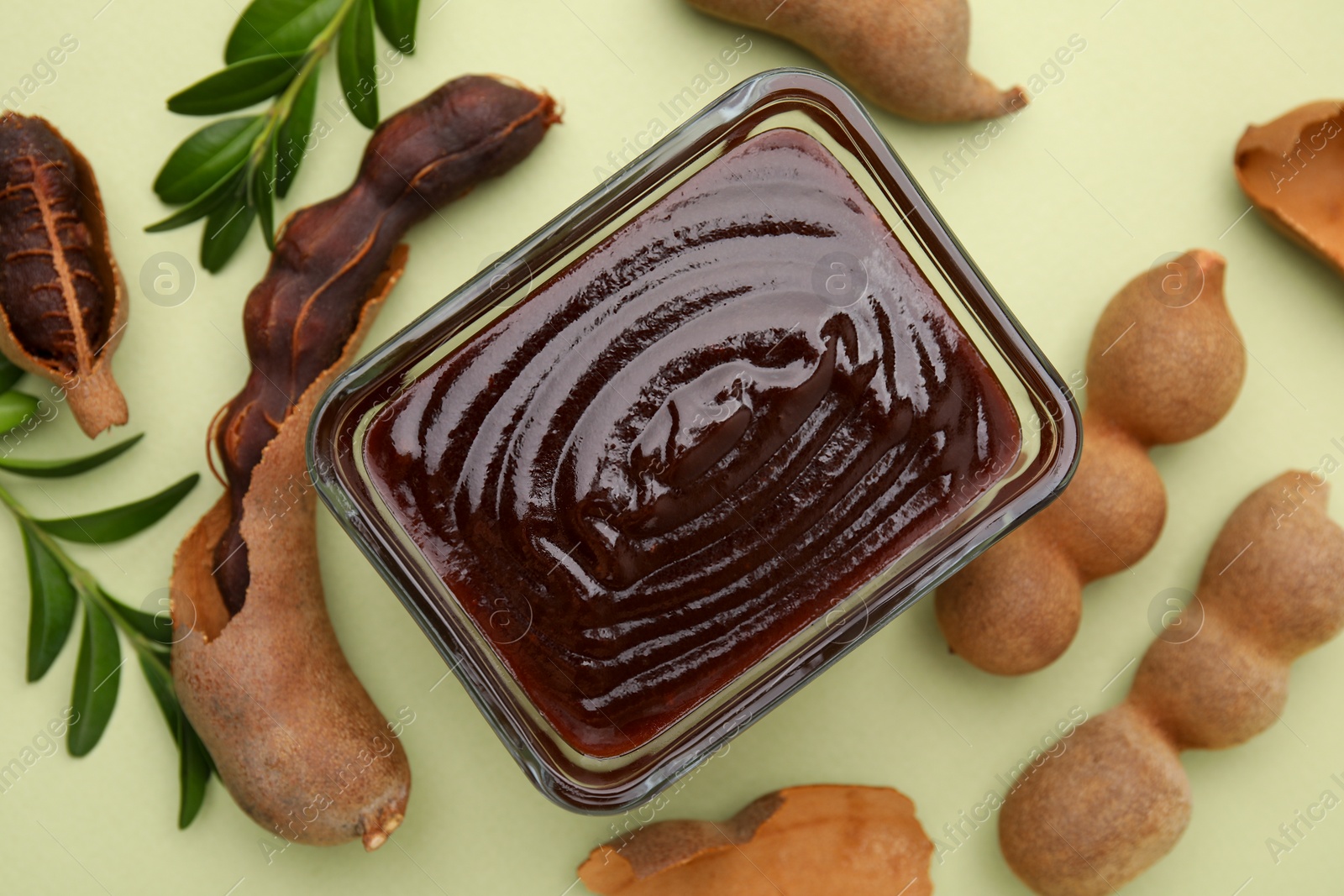 Bowl of tasty tamarind sauce, leaves and fresh pods on light green table, flat lay Photo of Bowl of tasty tamarind sauce, leaves and fresh pods on light green table, flat lay