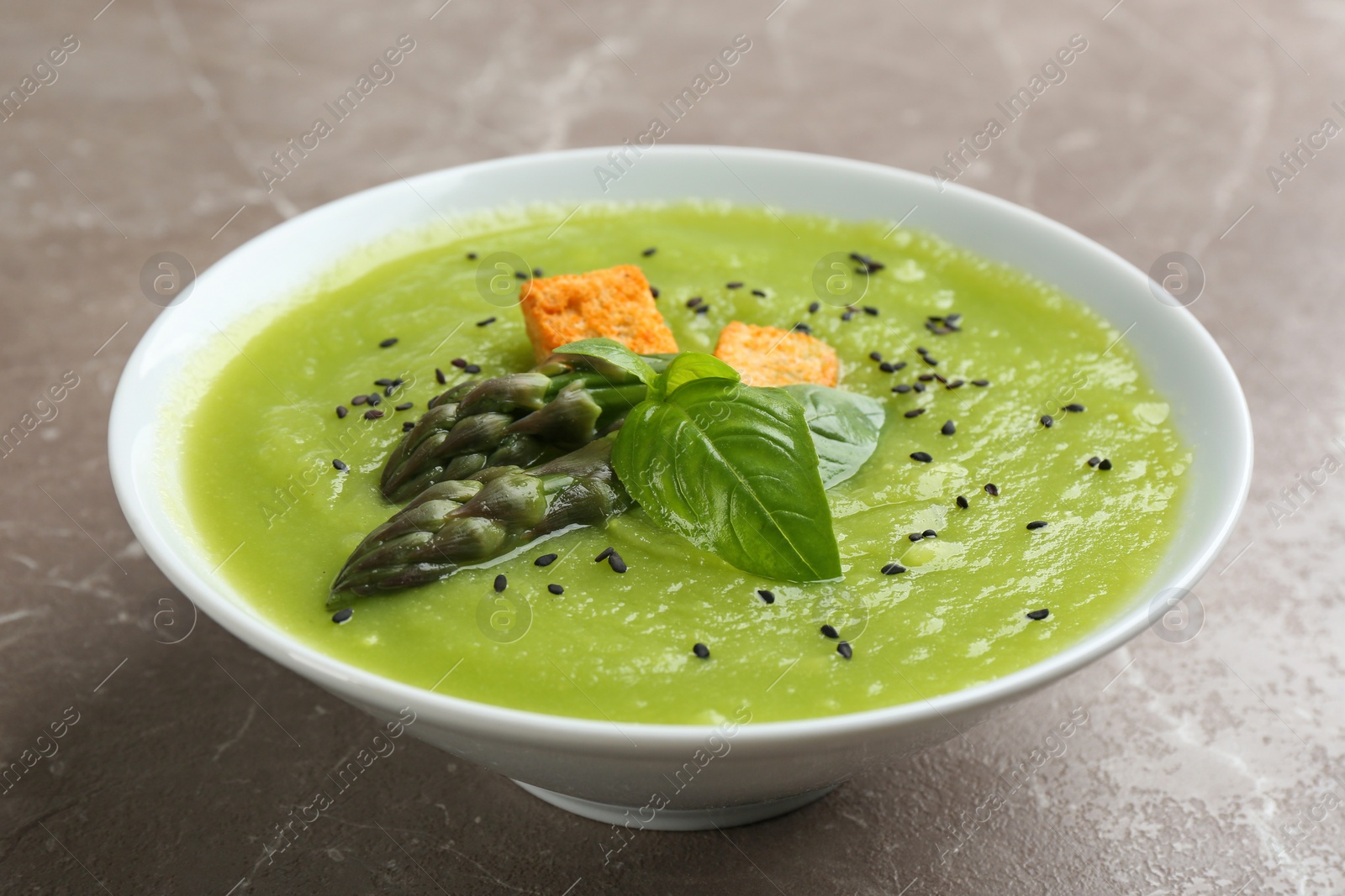 Photo of Delicious asparagus soup in bowl on grey marble table