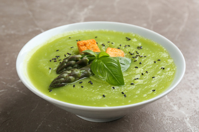 Photo of Delicious asparagus soup in bowl on grey marble table